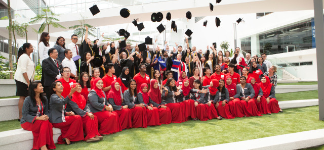 A group of students wearing red robes at their graduation. Some of them have thrown their caps into the air. 