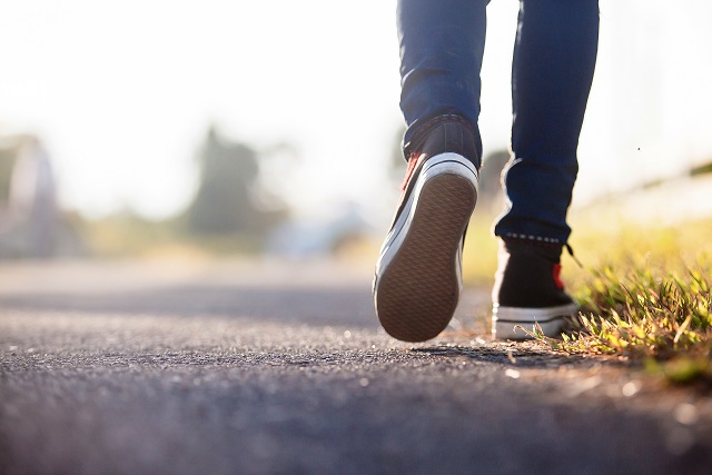 Ground-level view of back of person's legs walking down a path