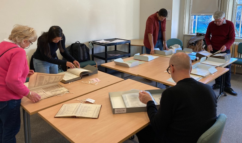 Five volunteers around a table reading books and letters from the archive.